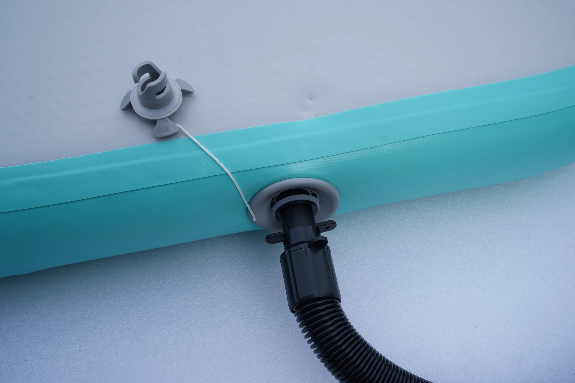 Close-up of an inflatable paddleboard's air valve with an attached hose and teal sidewall, used for inflation or deflation.