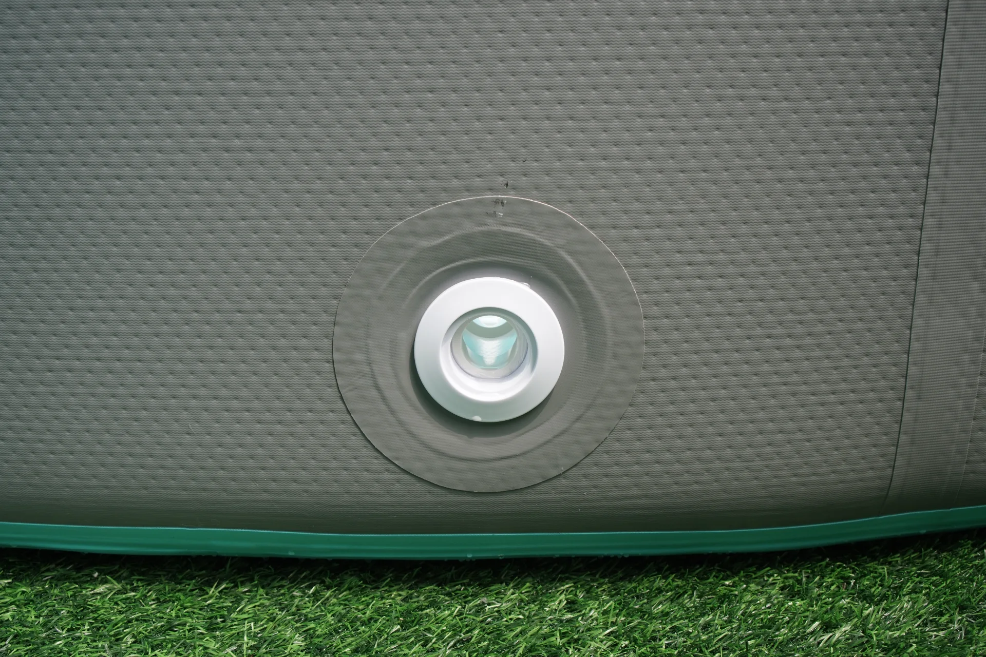 Close-up image of an inflatable pool's air valve on a textured gray surface, positioned on artificial green grass.