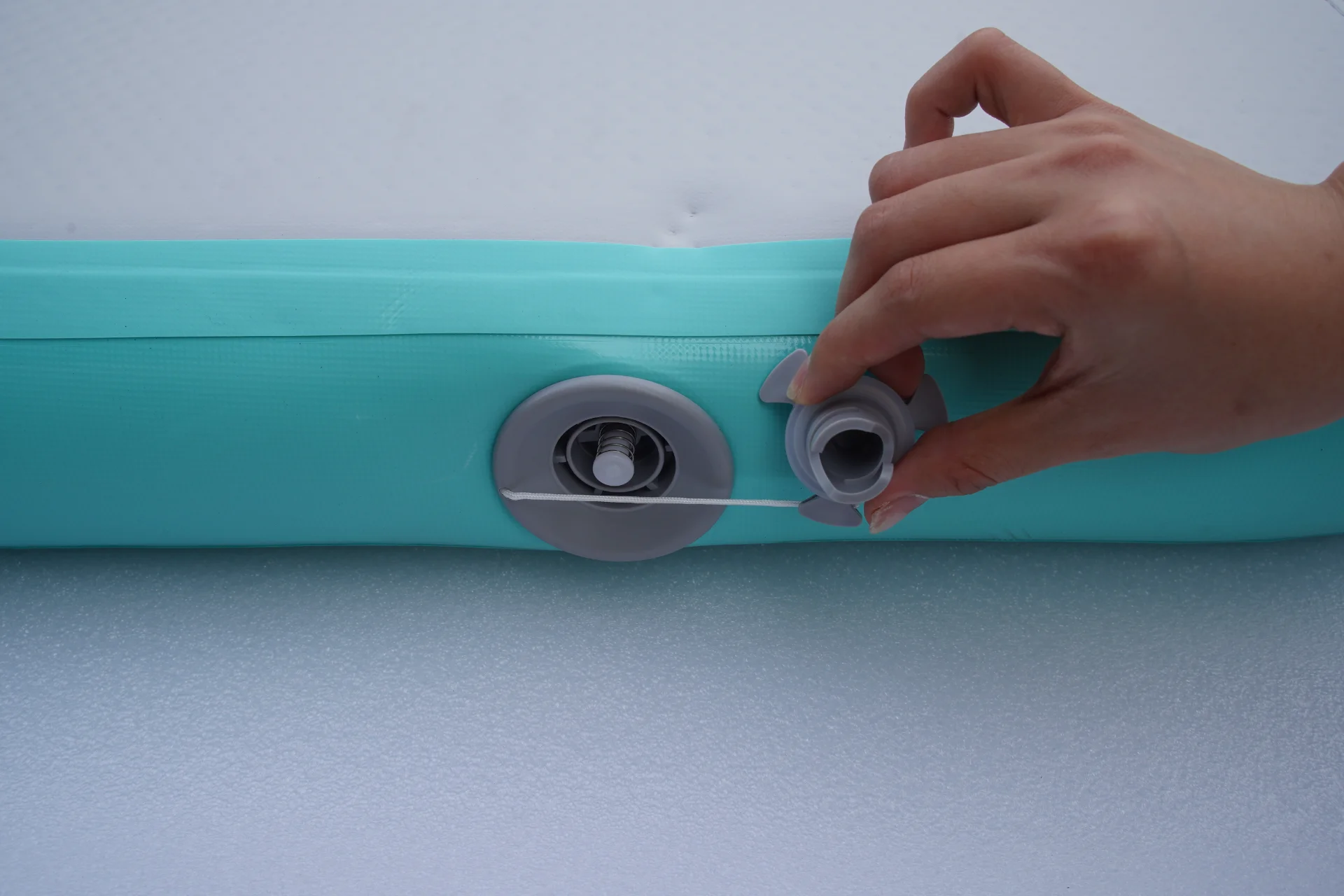 Close-up of a hand operating a valve on a turquoise inflatable surface, showing the attachment and removal of the valve cap.