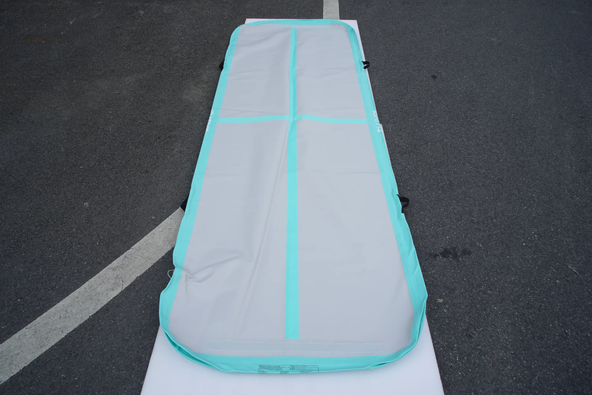 Outdoor padded mat with a grey surface and teal border laid on asphalt pavement.