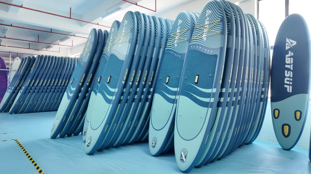 Rows of blue paddleboards neatly stacked in a factory setting with bright lighting.