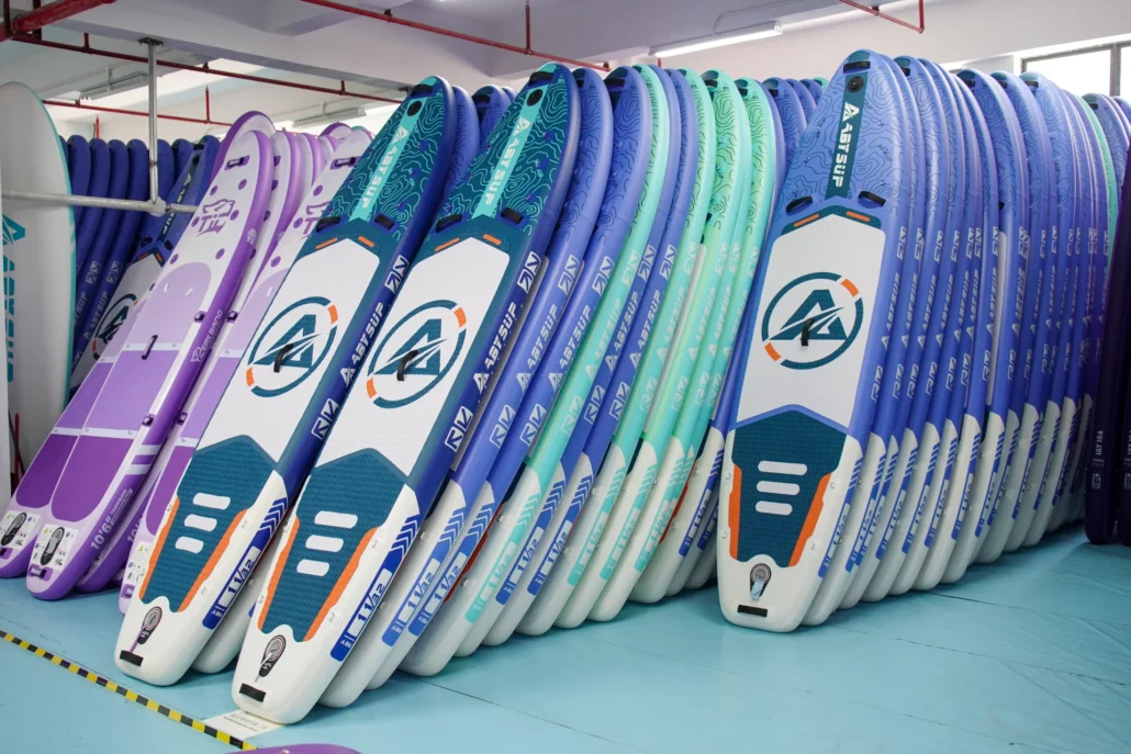 Rows of colorful paddleboards neatly stacked in a display, featuring blue, purple, and white designs with branded logos.