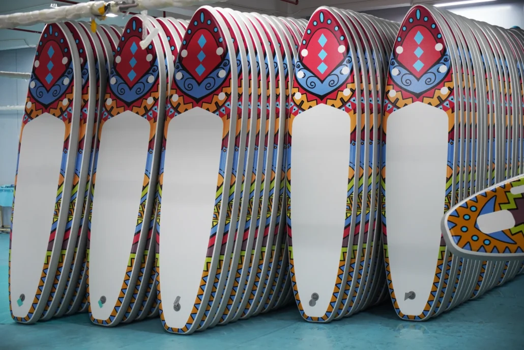 Multiple white paddleboards with colorful, tribal-inspired designs stacked neatly in a storage space.
